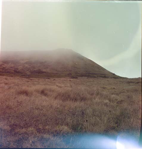 A hazy view of a hill in the distance. The top is covered with fog.