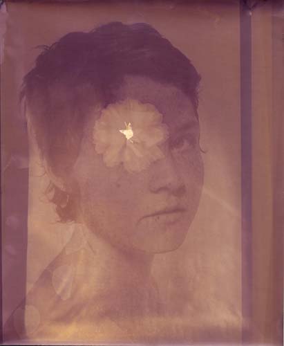 A close up three quarters portrait of a model, her gaze towards the camera. Her right eye has been contact printed with a flower, and the impression of petals can be seen.
